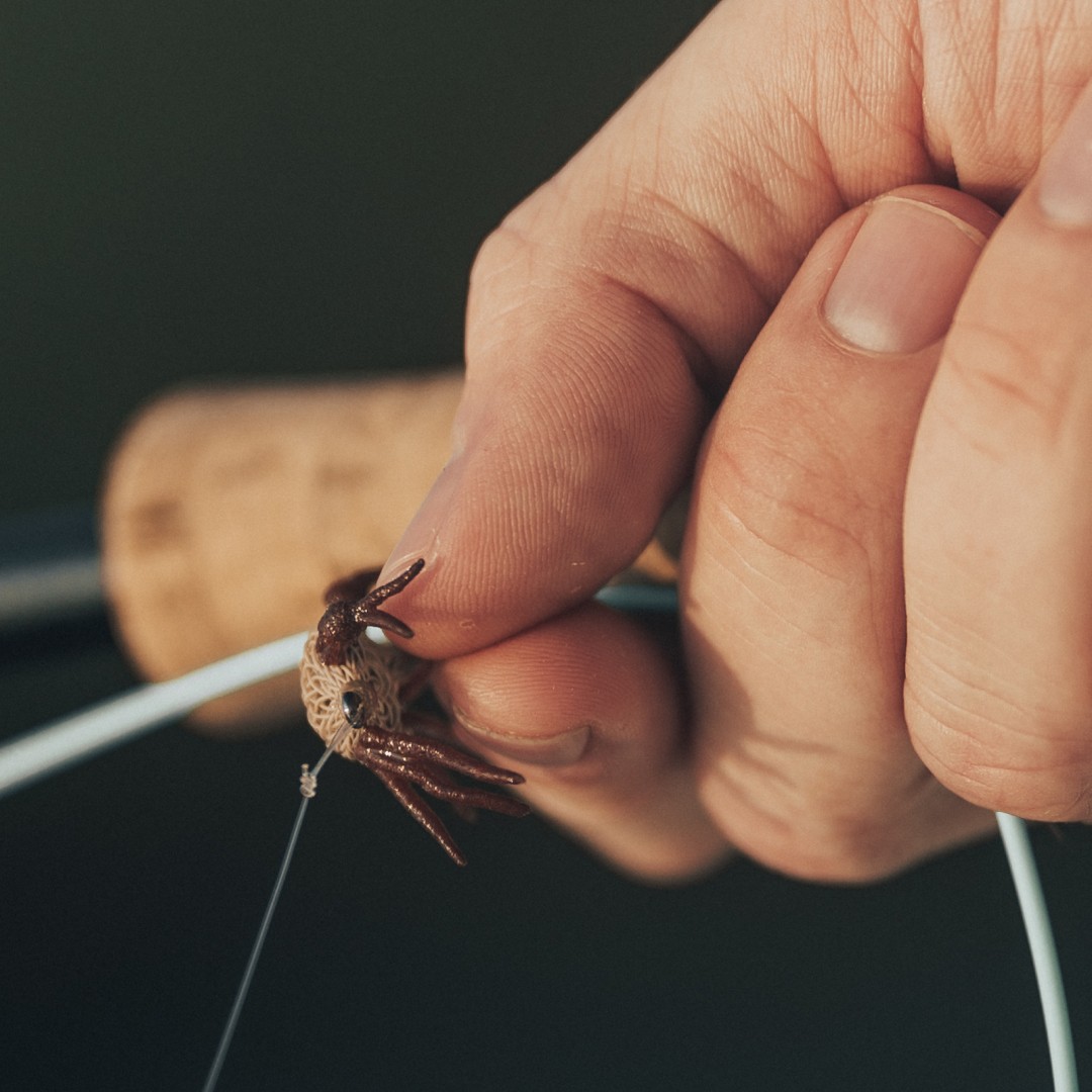 Closeup of a hand holding a fly fishing rod and a flexo crab fly